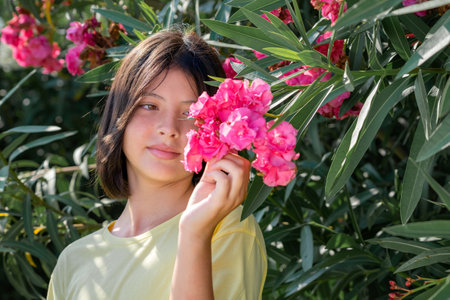 A cute little girl standing against a background of greenery holds pink flowers in her hand.の写真素材