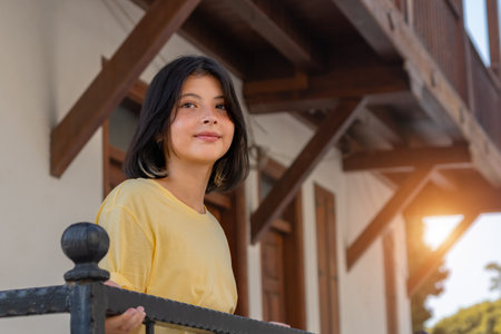A teenage girl with dark hair stands on the balcony of a country house.の写真素材