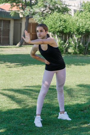 The girl kneads her back in a city park on a sunny day. physical exercise outdoors.の写真素材