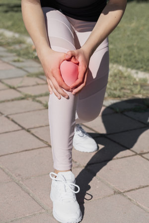 The girl holds an injured knee joint in her hands. Injury while running outdoors.の写真素材