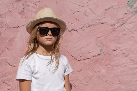 A preteen girl with blond hair poses for the camera against a pink wall.の写真素材