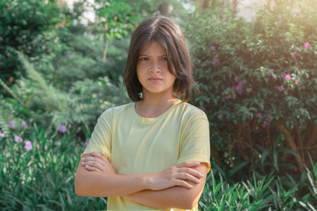 Half-length portrait of a young girl with crossed arms, frowning discontentedly. A teenager on a background of green vegetation.の写真素材