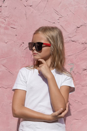 A preteen girl with blond hair poses for the camera against a pink wall.の写真素材