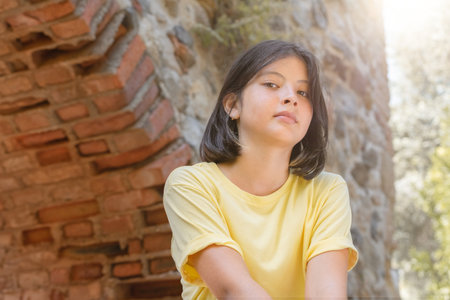 Portrait of a young girl on the background of a stone wall with an arch. A girl with dark hair poses for the camera. Low viewing angle.の写真素材