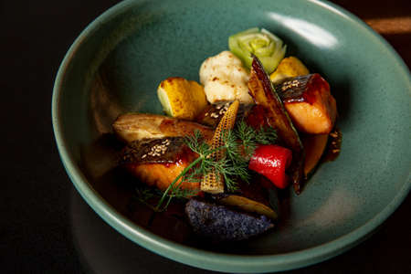 Teriyaki salmon with vegetable stew in the fine dining Japanese restaurant in a fine green bowl, with baby corn, pumpkin, red capsicum pepper and a vegetable flowerの写真素材