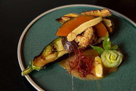 Kaiseki dish on the fine green plate in the fine dining Japanese restaurant, dark background, made with roast eggplant with pumpkin vegetable.の写真素材