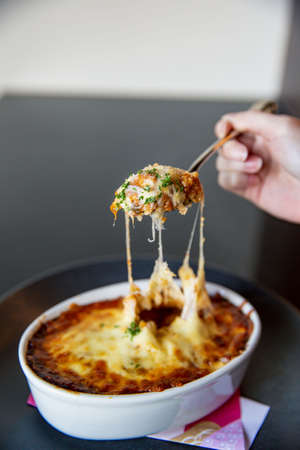 Tomato cheese risotto with spoon melting cheese in the kaiseki fine dining Japanese restaurant, with a fine black plate in black scene backgroundの写真素材