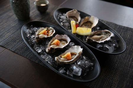Fresh oysters appetizer with sauce and lemons in the traditional Japanese ramen restaurant, with a black plate on a black mat in a black scene backgroundの写真素材