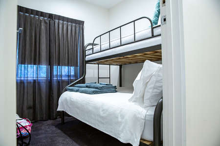 Bright white modern interior with dual-layered bunk bed, grey curtain and travel suitcase in accommodation hostel hotel holiday stay, with bedding, pillows, green blanketのeditorial素材