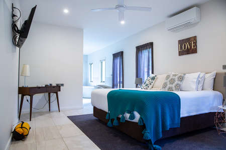 Bright white modern interior bedroom with opening bathroom in accommodation hostel hotel holiday stay, with king-size bedding, wooden drawer, pillows, green blanketのeditorial素材