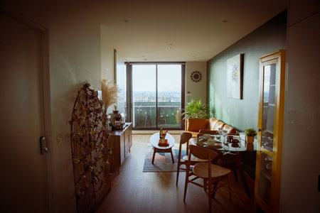 Dark vibe vintage interior living room with retro furniture in accommodation hostel hotel holiday stay, with orange sofa, wooden dining chairs, shelves, balcony and green plantsのeditorial素材