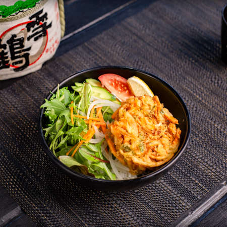 Veggie vegan tempura don with salad in the traditional Japanese ramen restaurant, with a black bowl on a black mat and Japanese fonts sake barrel translation: Snow Craneの写真素材