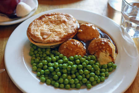 Australian traditional meat pie with meat gravy, mash potato, green peas on a white plate in restaurant in Australiaの写真素材