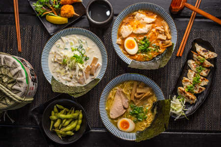Ramen combo platter with Pork tonkotsu chashu ramen, soy ramen, crab claw, edamame soybeans, spicy fried pork gyoza dumplings on black table, Top viewの写真素材