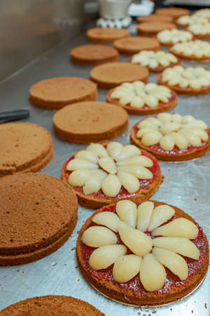 Patissier making pear cake sponge cake bases with raspberry jam in a traditional European bakery kitchenの写真素材
