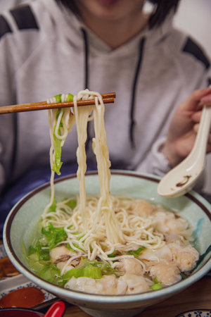 Hungry Customer Using Chopsticks to Pick up Delicious Wonton Soup Noodles in a Restaurantの写真素材