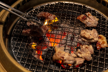 Expertly grilled flank skirt chicken slices skillfully flipped over a glowing charcoal grill in a vibrant yakiniku restaurant for Japanese or Korean BBQの写真素材