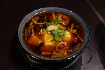 Aromatic Chinese Hot and Sour Soup Served in a Traditional Blue Bowl with Tofu and Mushroom Garnishの写真素材