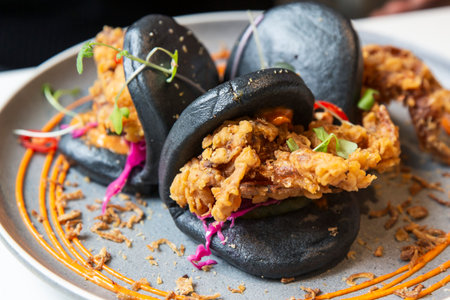 Charcoal-Black Bao Buns with Crispy Soft Shell Crab, Vibrant Veggies, and Savory Sauces on a Slate Plateの写真素材