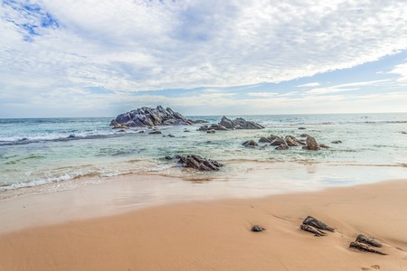 Beautiful lanscape of a sandy beach with rocks in the ocean against a blue sky background.の写真素材