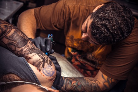 Tattoo master at work in tatoo salon./Man wearing gloves showing process of making a tattoo in tattoo parlor.の写真素材