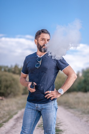 Stylish brutal vape man enjoying an vape out in the forest. The new technology cigarette.