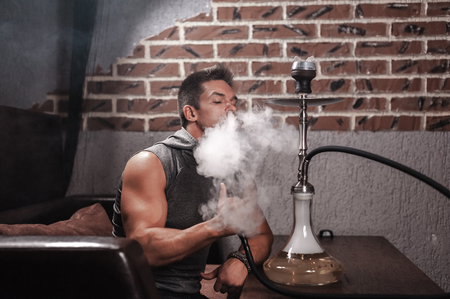 Man smokes a fragrant oriental hookah in nightclub.