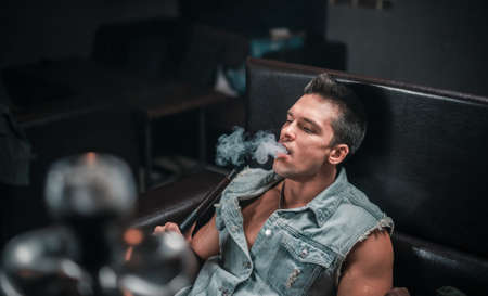 Sexy guy smokes a fragrant oriental hookah at arabic restaurant.の写真素材