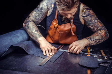 Leather Craftsman cuts out leather goods in workplaceの写真素材
