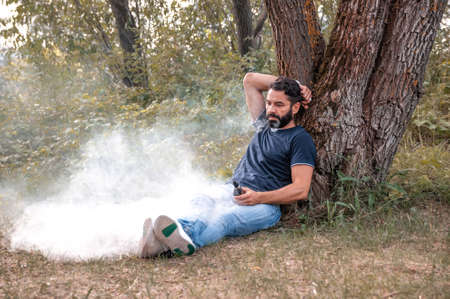 Bearded smoker smoking an electronic smoke device outdoorr. Man really likes process of smoking.
