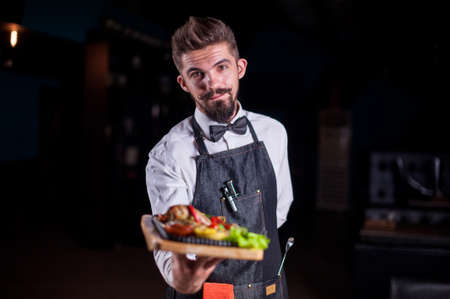 Professional friendly flunky helpfully holds plate with prepared dish at a festive event.の写真素材