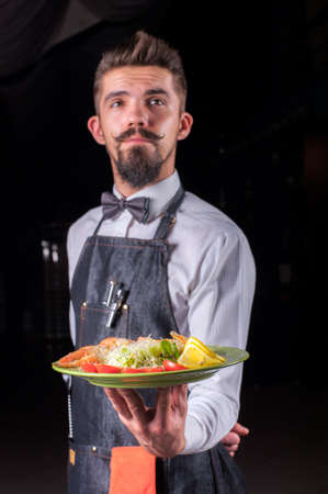 Whiskered waiter helpfully serves plate with prepared dish at a festive event.の写真素材