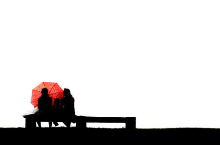 Silhouette of parents with child behind umberella sitting on benchの写真素材