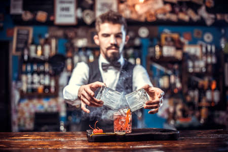 Confident barman adds ingredients to a cocktail while standing near the bar counter in nightclubの写真素材