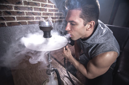 Young fellow relaxes in a hookah in cafe.
