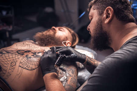 Master of the art of tattooing makes a tattoo on the skin in tattoo parlorの写真素材