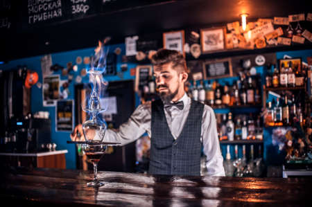 Young bartending pouring fresh alcoholic drink into the glasses on the barの写真素材