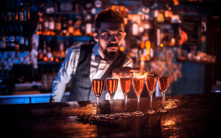 Charismatic bartending pouring fresh alcoholic drink into the glasses behind the barの写真素材