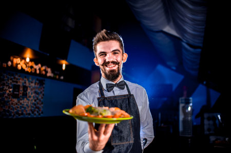 Stylish waiter holds plate with prepared dish on a black background.の写真素材