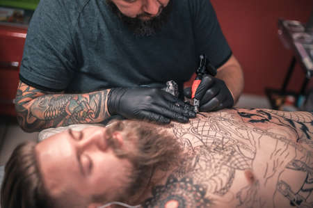 Master tattooist makes a tattoo on the skin in a workshop studioの写真素材