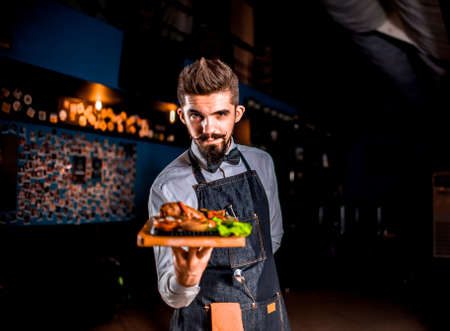 Professional friendly waiter serves appetizing dish on a black background.の写真素材