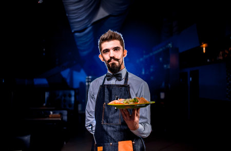 Charismatic waiter serves plate with prepared dish in the restaurant.の写真素材