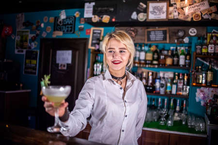 Focused woman bartender pouring fresh alcoholic drink into the glasses at the night clubの写真素材