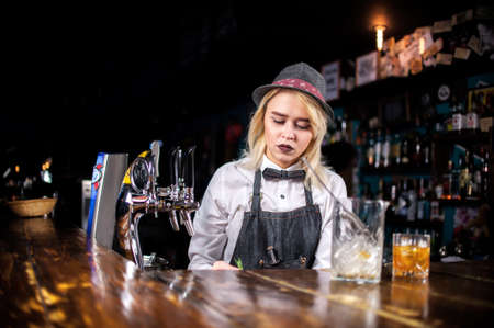 Confident girl bartender pouring fresh alcoholic drink into the glasses at barの写真素材