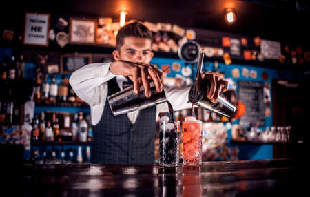 Experienced barkeeper mixes a cocktail while standing near the bar counter in barの写真素材