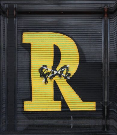 closeup full view of huge capital letter R  in yellow paint on shutter doors on a dark background into shapes patterns and intricate designsの写真素材