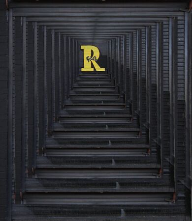 closeup of diminishing perspective concentric surface view of huge capital letter R  in yellow paint on shutter doors on a dark background into shapes patterns and intricate designsの写真素材