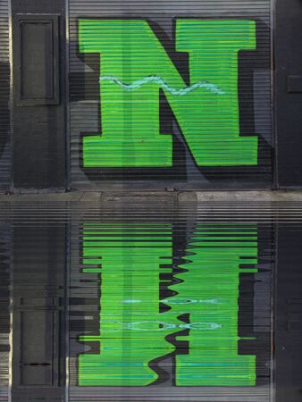 water reflection ripple effect of huge capital letter N  in green paint on shutter doors on a dark background into shapes and patternsの写真素材
