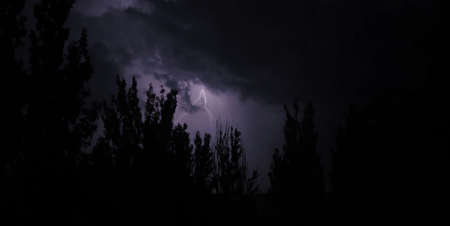 Streaks of bright lightening bolts rip through the purple night sky on a city street with a...