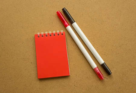Red notepad for notes with red sheets. Blank space for notes. Mocap. Two felt-tip pens in red and black. On a warm ocher gray background. Holiday calendar notes on notepad. background for inscriptionsの写真素材